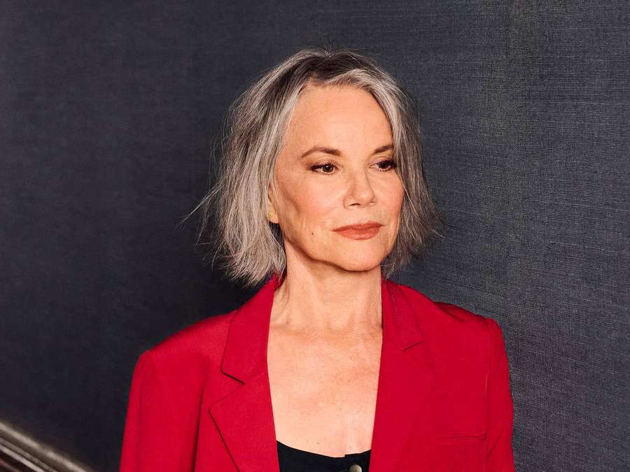A woman with gray hair in a red blazer looks thoughtfully to the side. — Barbara Hershey Wallpaper