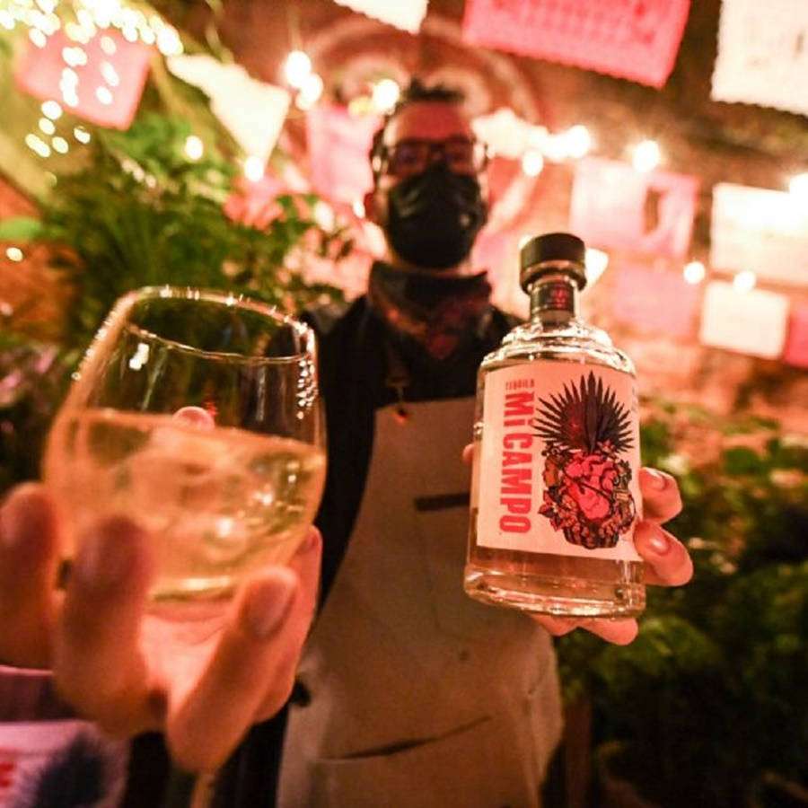 Barkeeper mit Maske hält Tequilaflasche und Cocktailglas unter Lichterketten. — Barkeeper Wallpaper