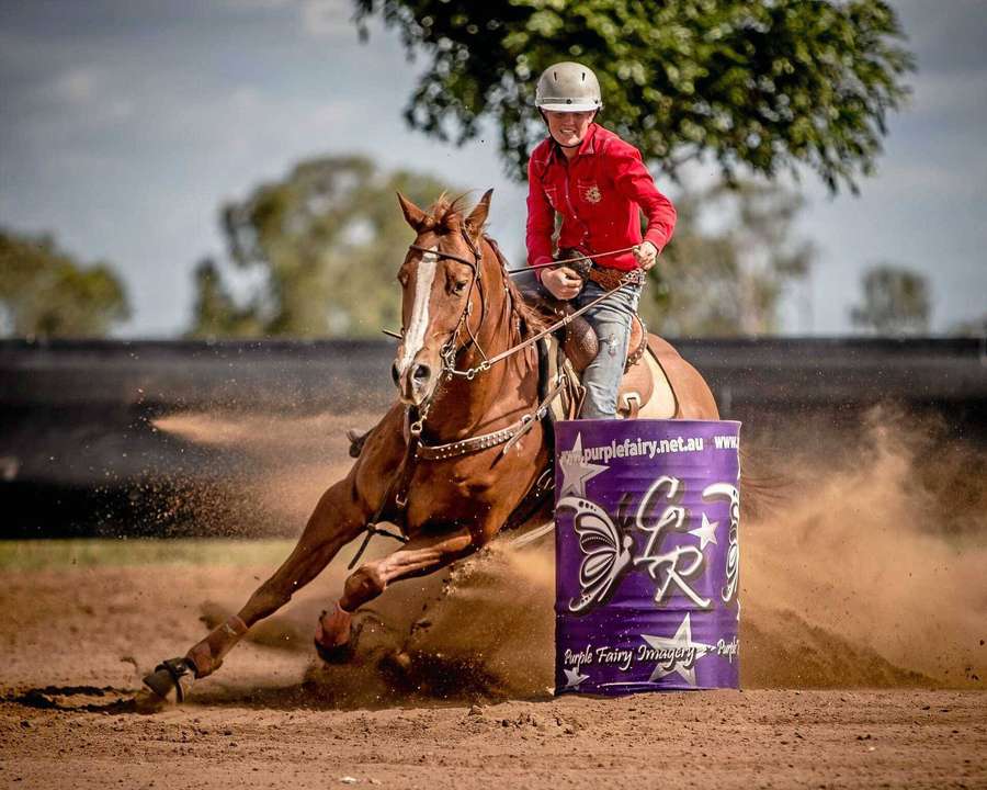 A rider on a horse rounding a purple barrel in a dusty arena. — Barrel Racing Wallpaper