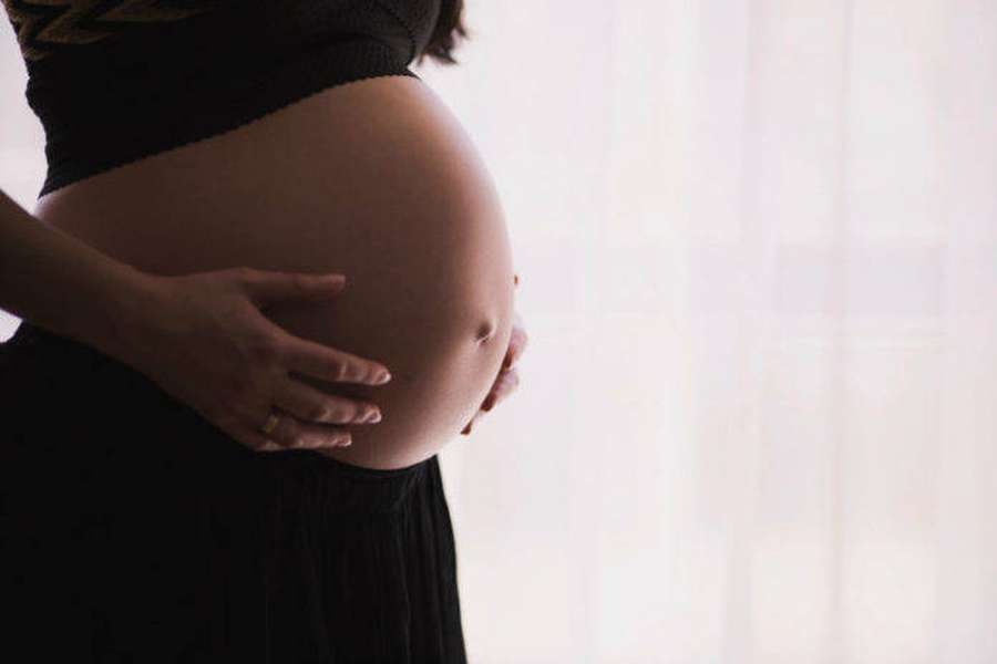 Uma mulher grávida segura a barriga com as duas mãos perto de uma janela. — Barriga de grávida Papéis de Parede