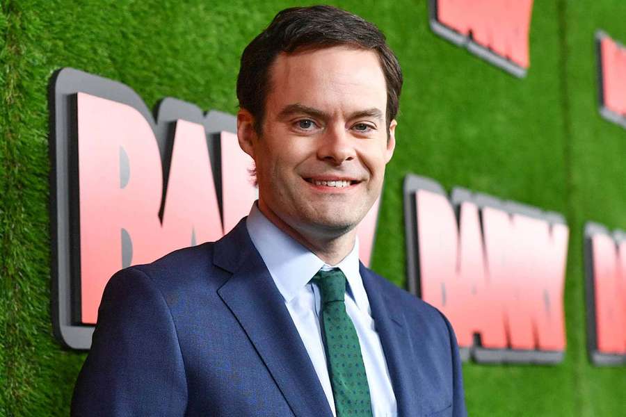 Man in blue suit and green tie smiling at event with green wall and pink text behind him. — Barry Background