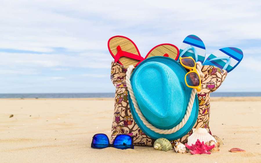 Beach bag with flip flops sunglasses and seashells on sandy shore — Beach Bag Wallpaper