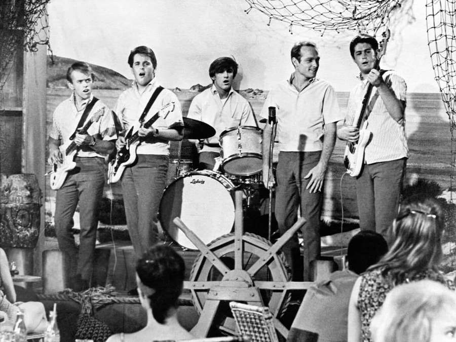 Five men playing music on a stage with an audience watching. — Beach Boys Wallpaper