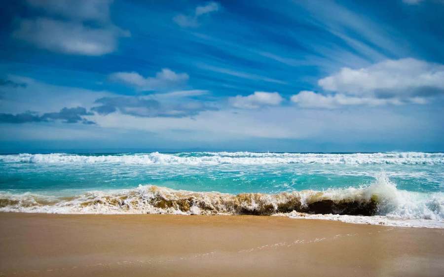 Turquoise ocean waves crashing on golden sand under a bright blue sky with white clouds. — Beach Desktop Background