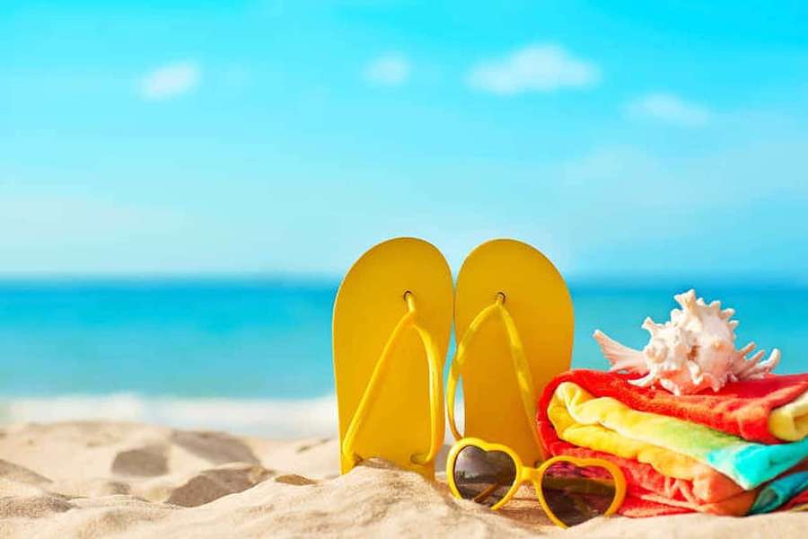 Yellow flip flops and heart sunglasses on beach with colorful towels and seashells. — Beach Sandals Wallpaper
