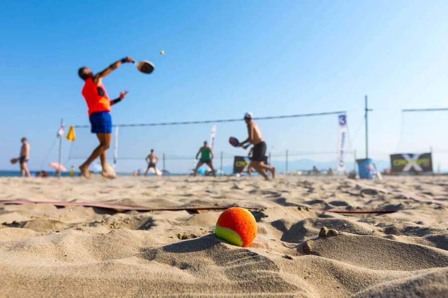 Pelota de tenis en la arena con jugadores en cancha de playa bajo el sol. — Beach Tennis Fondos de pantalla