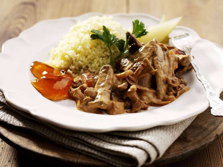 Tender meat in creamy sauce with couscous and orange jelly on a rustic wooden table. — Beef Stroganoff Background