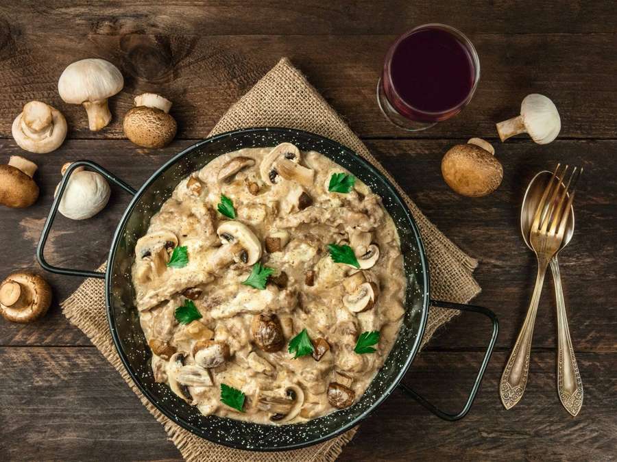 Creamy mushroom sauce in a pan with fresh parsley and scattered mushrooms on a wooden table. — Beef Stroganoff Wallpaper