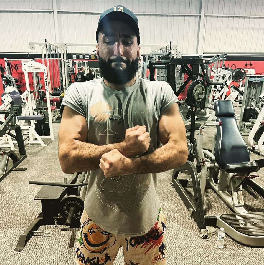 Bearded man flexing arms in gym with weight machines behind him — Belal Muhammad Wallpaper