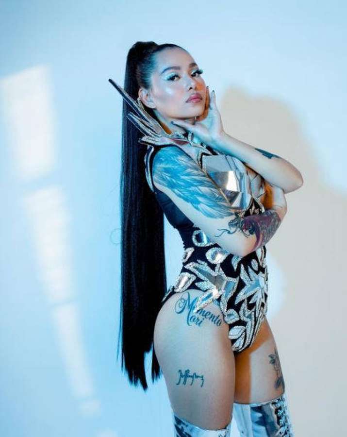 A tattooed woman in a metallic outfit posing in a studio with blue lighting. — Bella Poarch Wallpaper