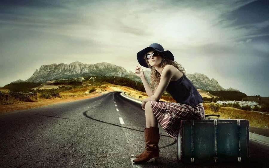 Mujer con maleta descansando al borde de la carretera cerca de montañas al atardecer — Belleza y moda Fondos de pantalla