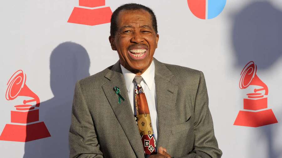 Man in suit holding Grammy award at event with red logos behind him. — Ben E King Wallpaper