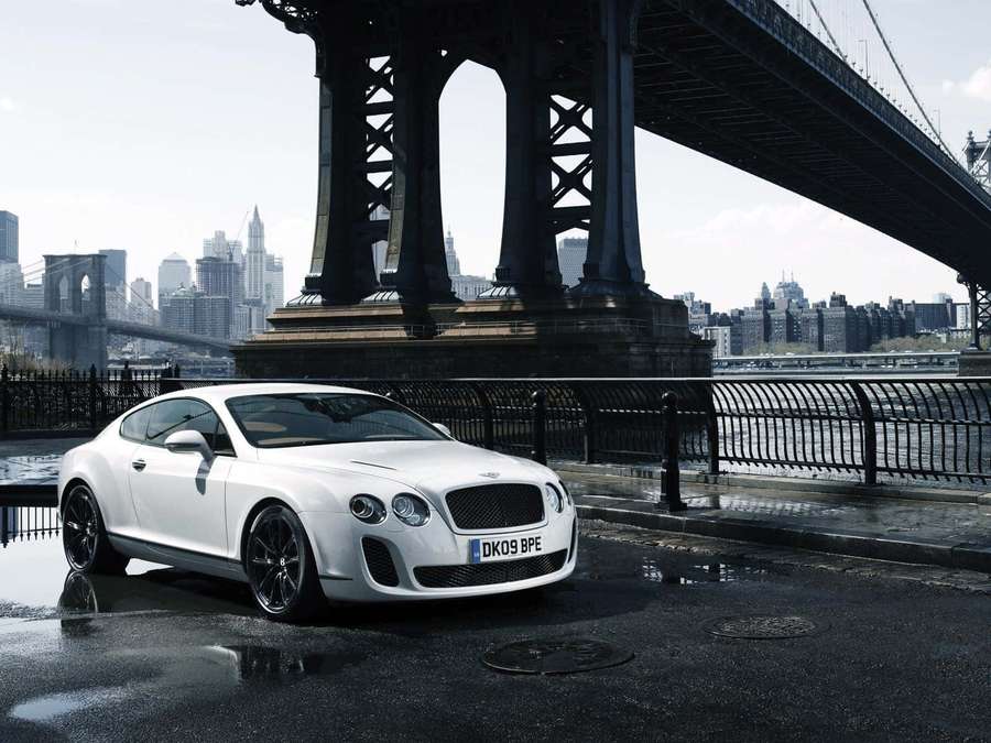 White Bentley sports car parked under Brooklyn Bridge on wet pavement. — Bentley Background