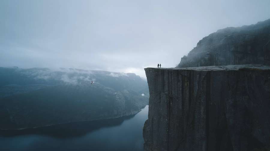 Zwei Personen auf einem Klippenrand über einem nebligen Fjord mit einem Bungee-Springer in der Luft. — Beste Qualität Wallpaper