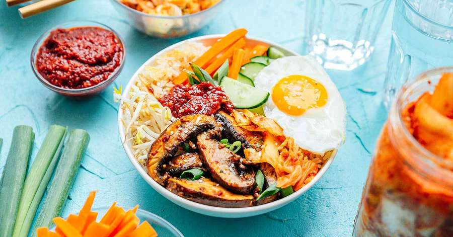 Bunte koreanische Bibimbap-Schale mit Ei, Kimchi und Gemüse auf türkisem Hintergrund — Bibimbap Bilder