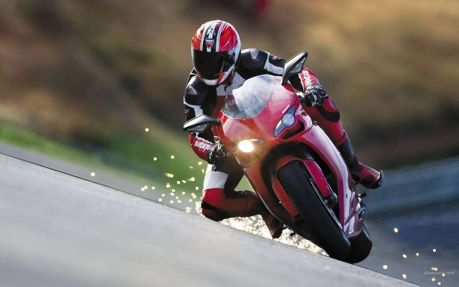 Motorcyclist leaning into a turn on a wet road with sparks flying. — Biker Picture