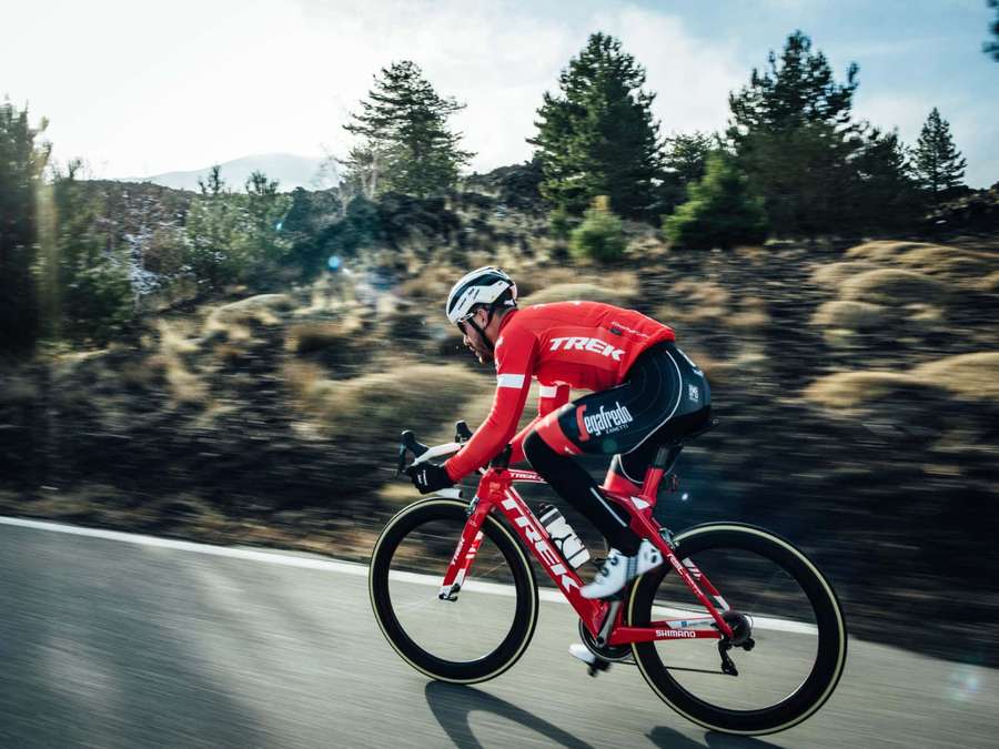 Cyclist in red Trek gear racing on mountain road with blurred background. — Bikes Background