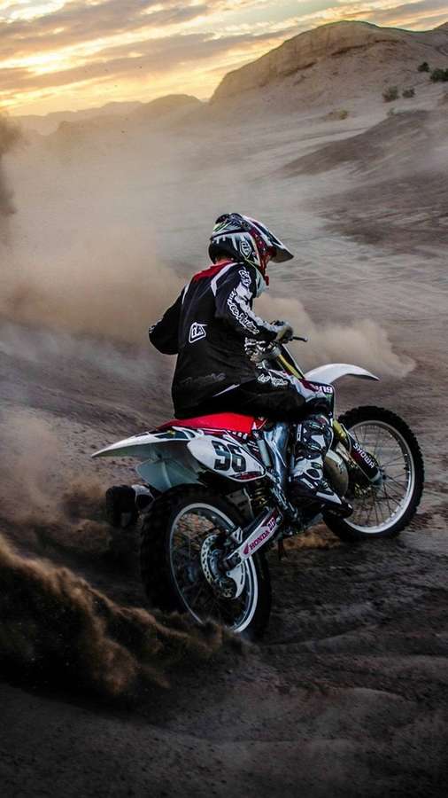 Motocross rider speeding through desert terrain at sunset kicking up dust. — Bikes iPhone Wallpaper