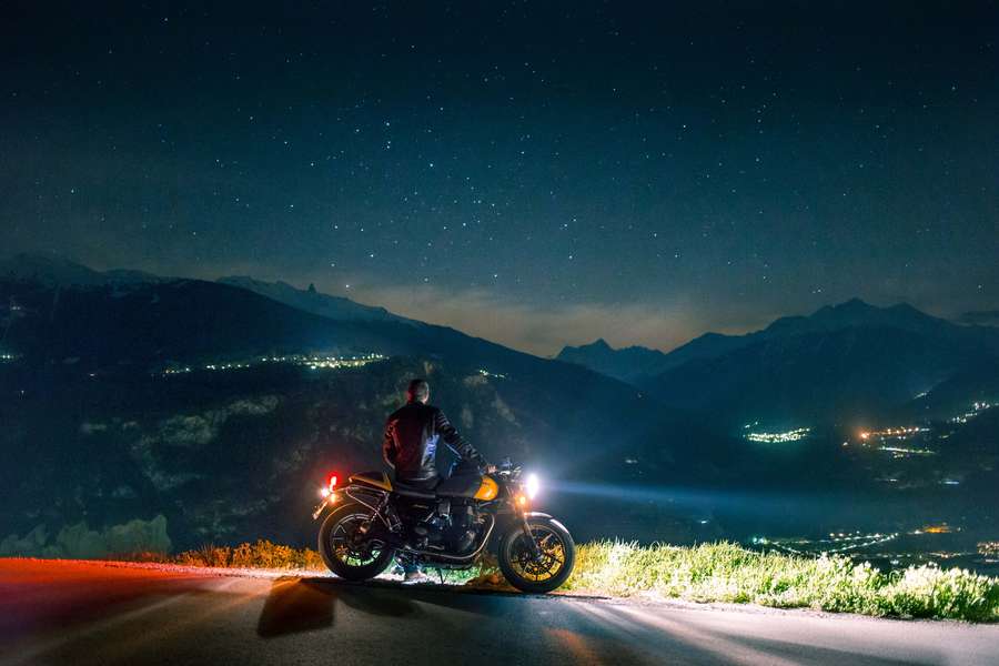 Motorradfahrer hält auf Bergstraße unter Sternenhimmel mit Lichtern im Tal. — Bilder Vom Hang Wallpaper
