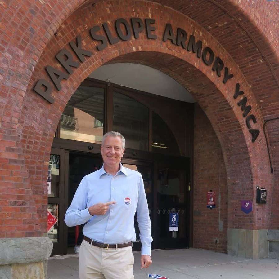 Man pointing to campaign button under Park Slope Armory YMCA brick archway. — Bill De Blasio Wallpaper