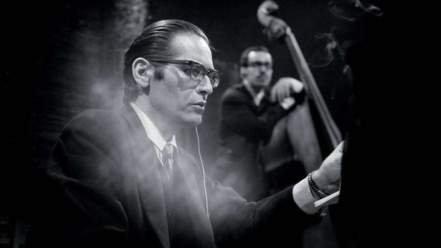 Jazz musician in suit and glasses playing piano in smoky studio. — Bill Evans Wallpaper