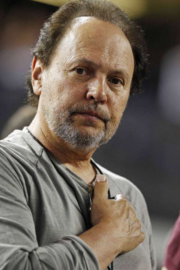 A serious man with a gray beard wearing a gray shirt with hand on chest. — Billy Crystal Background