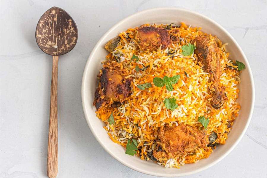 A bowl of chicken biryani with golden rice and mint garnish beside a wooden spoon. — Biryani Background