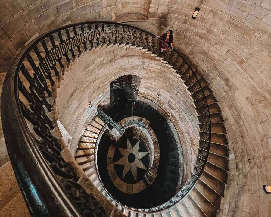 Mulher em pé em uma escada em espiral de pedra com corrimãos de ferro ornamentados. — Bispo Papéis de Parede