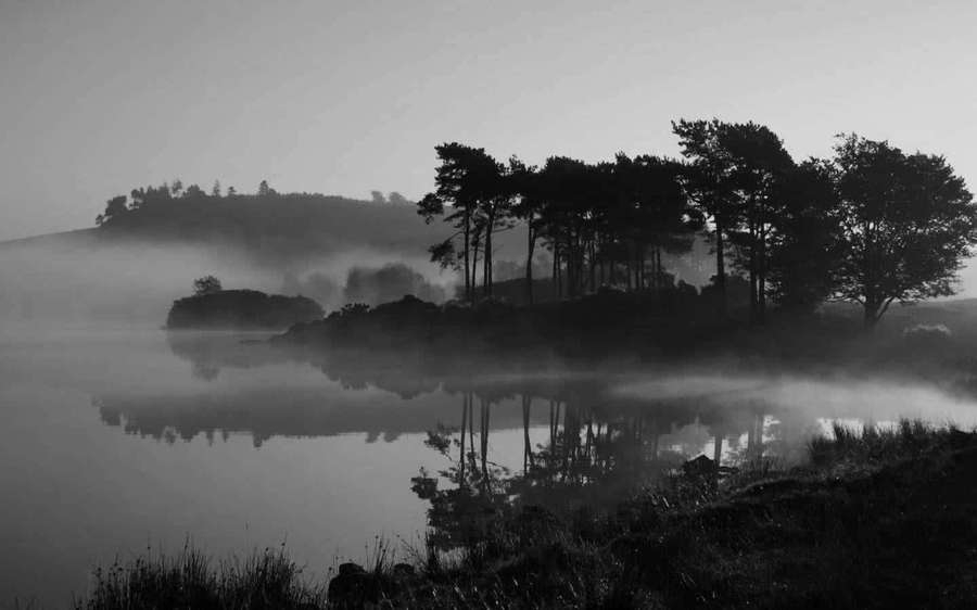 Silhouetted trees and hills reflected in a misty lake at dawn. — Black And White Landscape Wallpaper