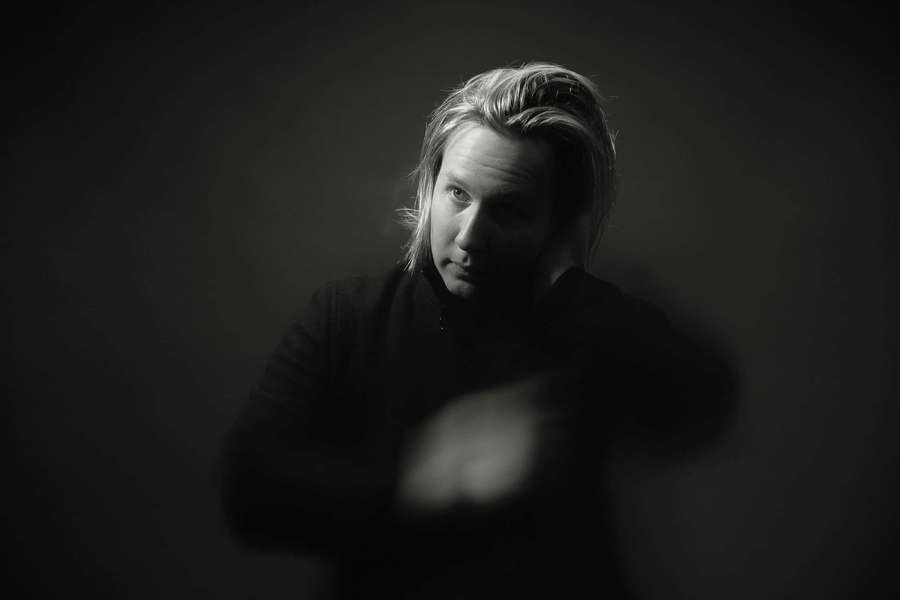 A person with tousled hair stares intently in a dark studio portrait. — Black Aura Wallpaper