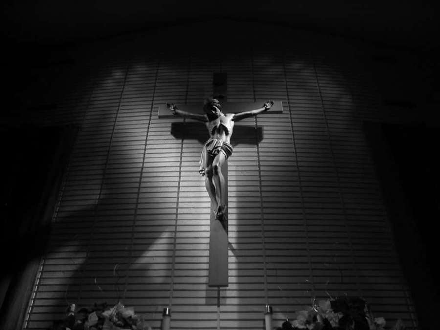 A lit crucifix statue on a slatted wall inside a church — Black Cross Wallpaper