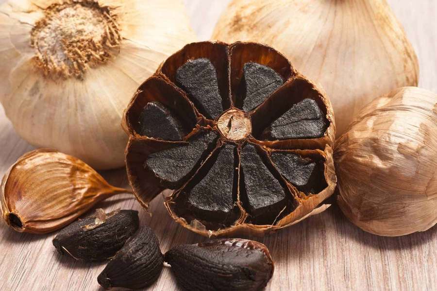 Black garlic cloves and whole bulbs on a wooden table — Black Garlic Wallpaper