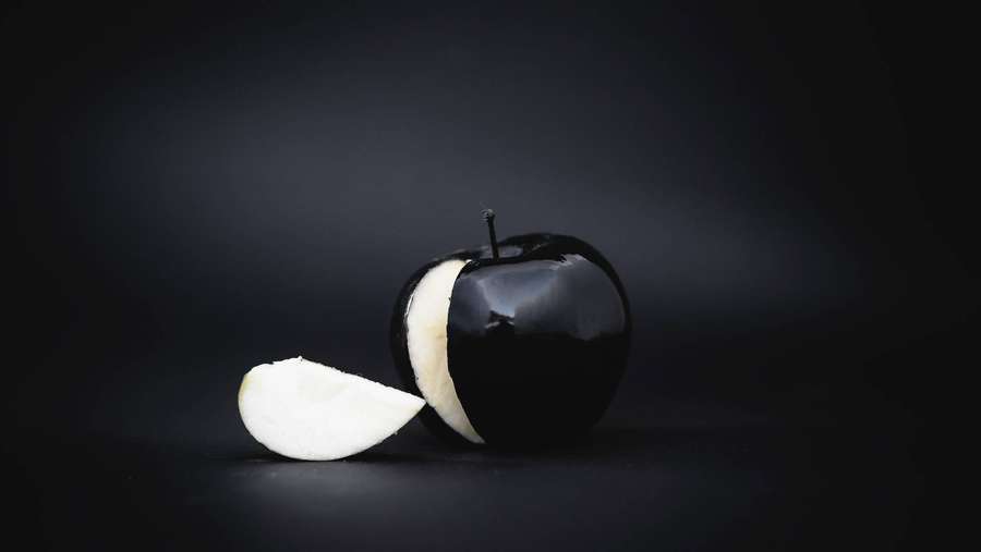 A black apple cut in half with white interior on a dark surface. — Black Pc Background