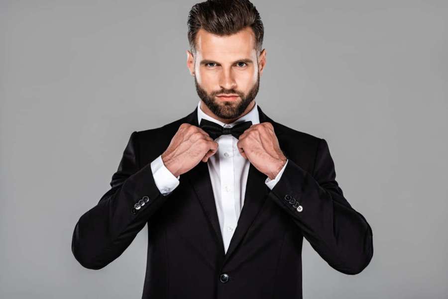 Handsome man adjusting his bow tie in a black tuxedo against gray background. — Black Tie Event Wallpaper