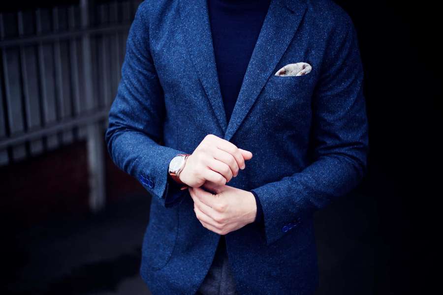 Man in blue blazer adjusting wristwatch in dim lighting. — Blazer Picture