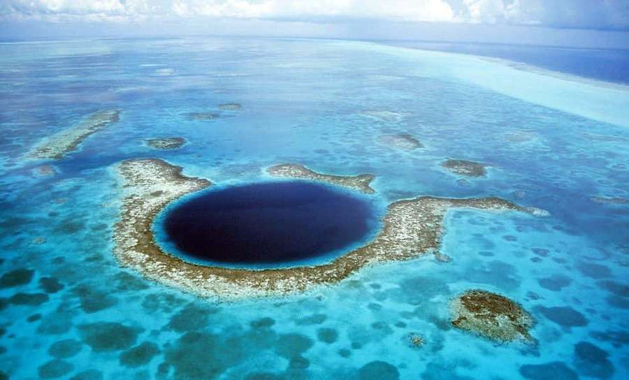Aerial view of a blue heart-shaped atoll surrounded by coral reefs and turquoise water. — Blue Hole Wallpaper