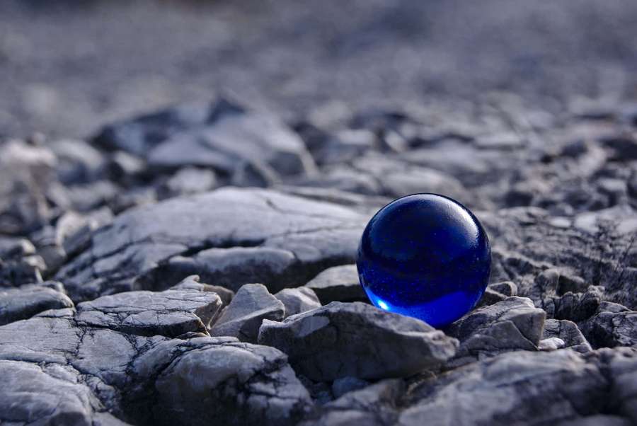 A blue glass sphere on cracked gray rocks in natural light. — Blue Marble Wallpaper