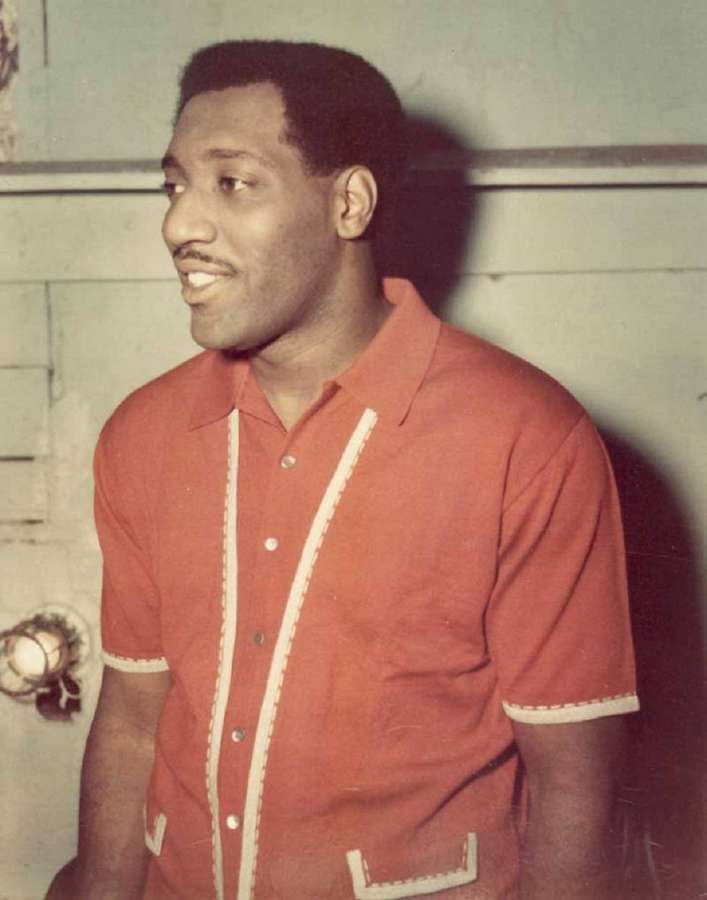 Un uomo sorridente con una camicia rossa con bordi bianchi in piedi all'interno. — Blues Sfondi