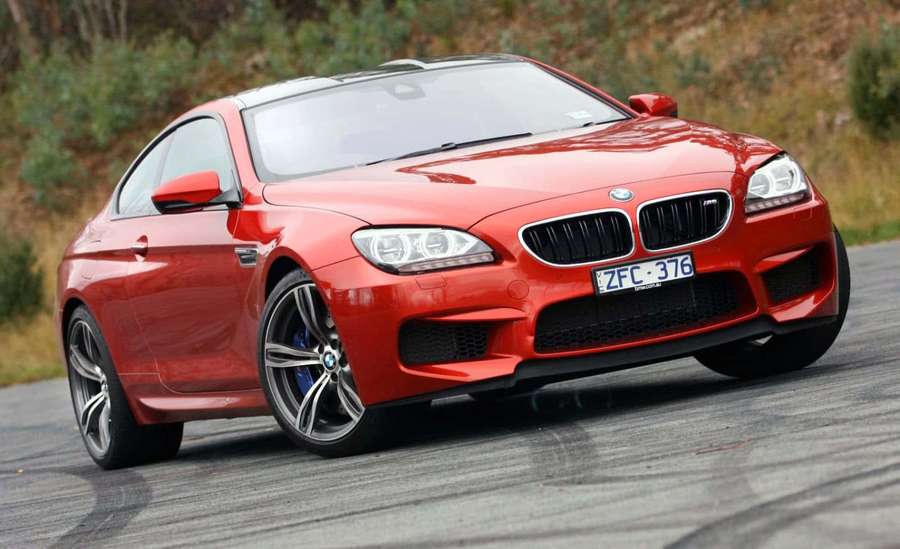 Rød BMW M6 sportsvogn kørende på en snoet vej omgivet af grønt. — Bmw M6 Wallpapers