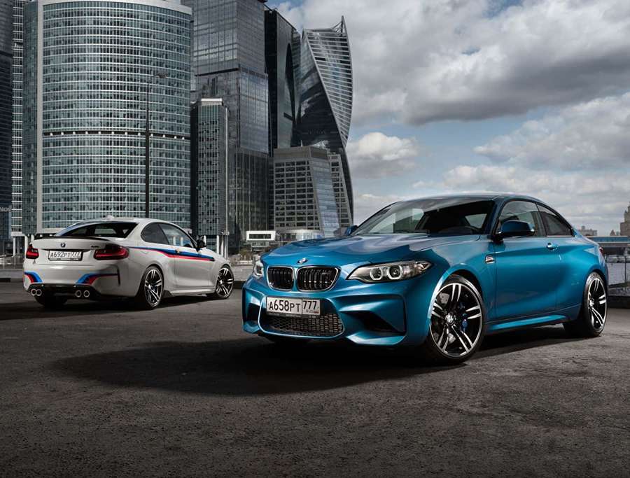 Two BMW sports cars parked in front of modern glass skyscrapers. — Bmw Tablet Wallpaper