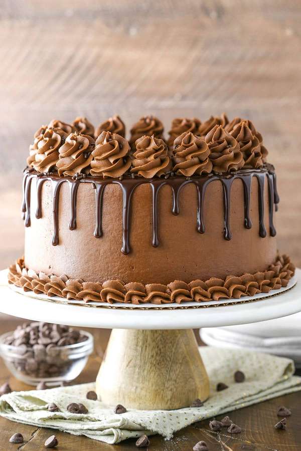 Um bolo de chocolate decadente com glacê de gotejamento e redemoinhos de confeitar em um suporte branco. — Bolo de chocolate Papéis de Parede