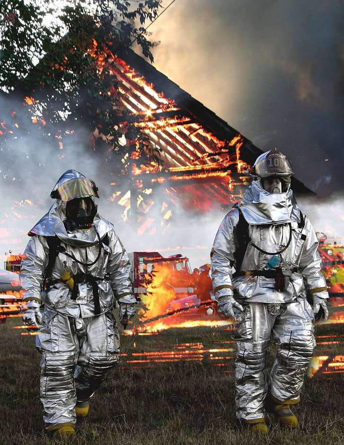 Dos bomberos completamente equipados caminando hacia una casa en llamas. — Bomberos Fondos de pantalla