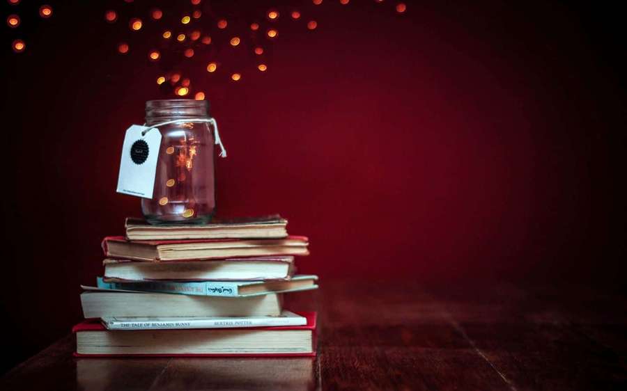 Stack of books with a lit jar on top against a red background. — Books Background