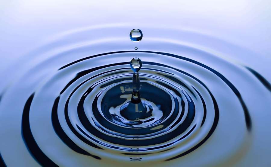 A water droplet poised above a rippling surface with concentric circles. — Bounce Wallpaper