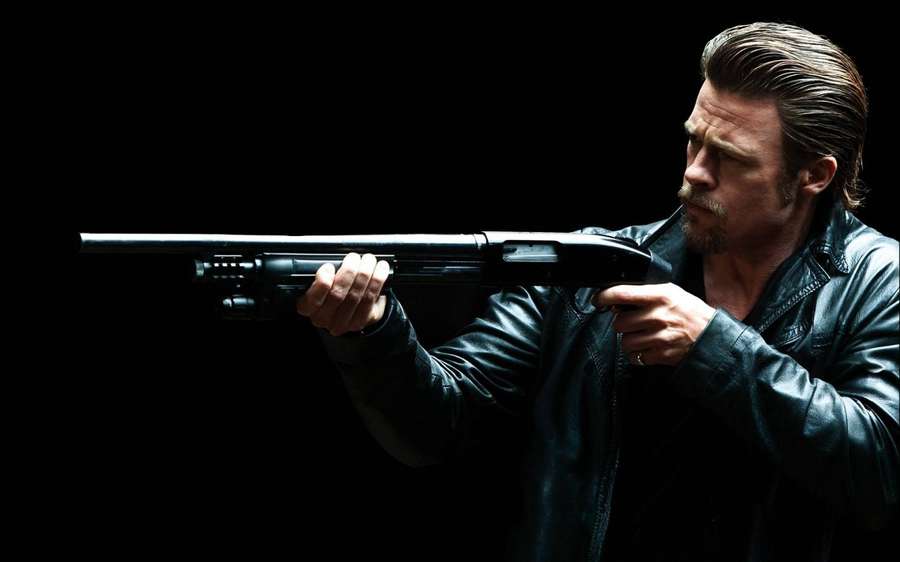 Brad Pitt zielt mit einer Schrotflinte in einer schwarzen Lederjacke vor einem dunklen Hintergrund. — Brad Bilder
