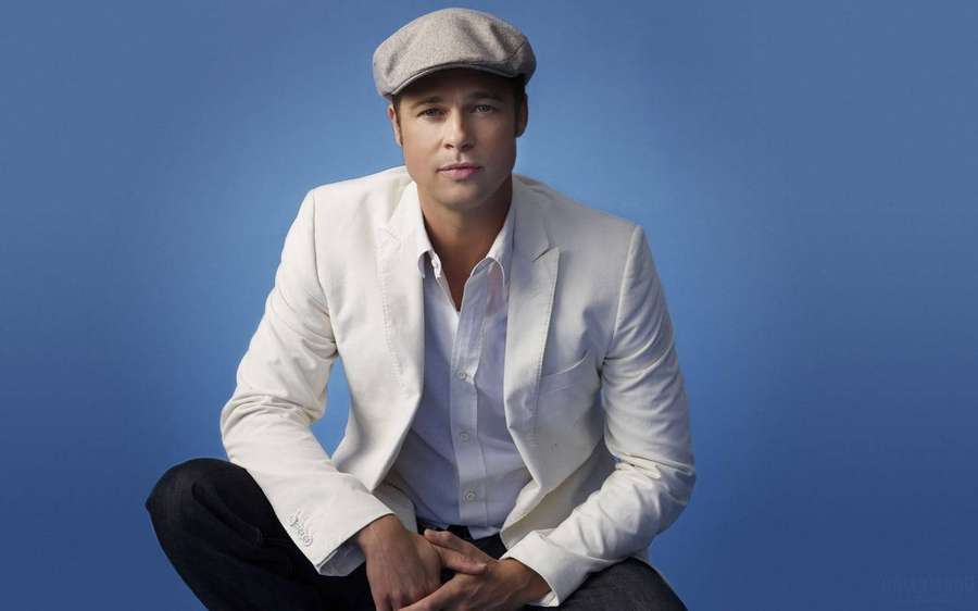 Man in white blazer and grey cap sitting against blue background. — Brad Wallpaper
