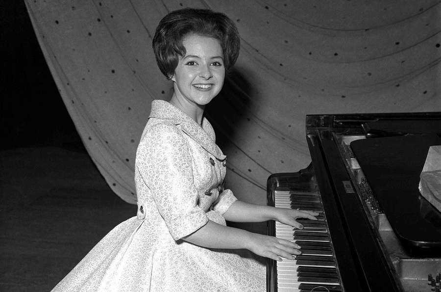 Young woman in floral dress smiling while playing grand piano in studio. — Brenda Lee Background