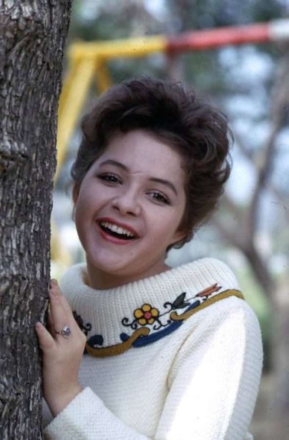 Eine lächelnde Frau in einem weißen Pullover lehnt sich im Freien an einen Baum. — Brenda Lee Bilder