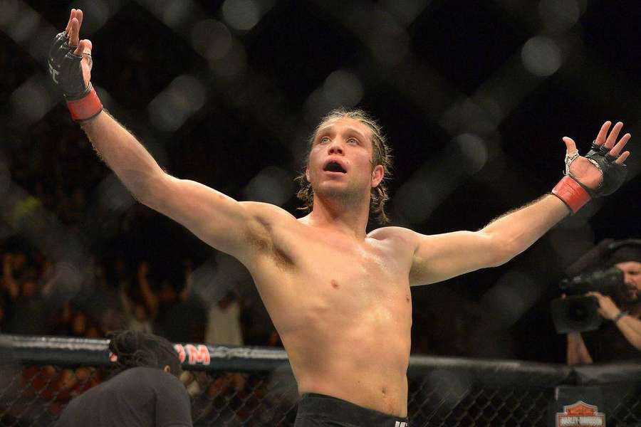 Lottatore di MMA festeggia la vittoria con le braccia alzate nell'ottagono. — Brian Ortega Sfondi
