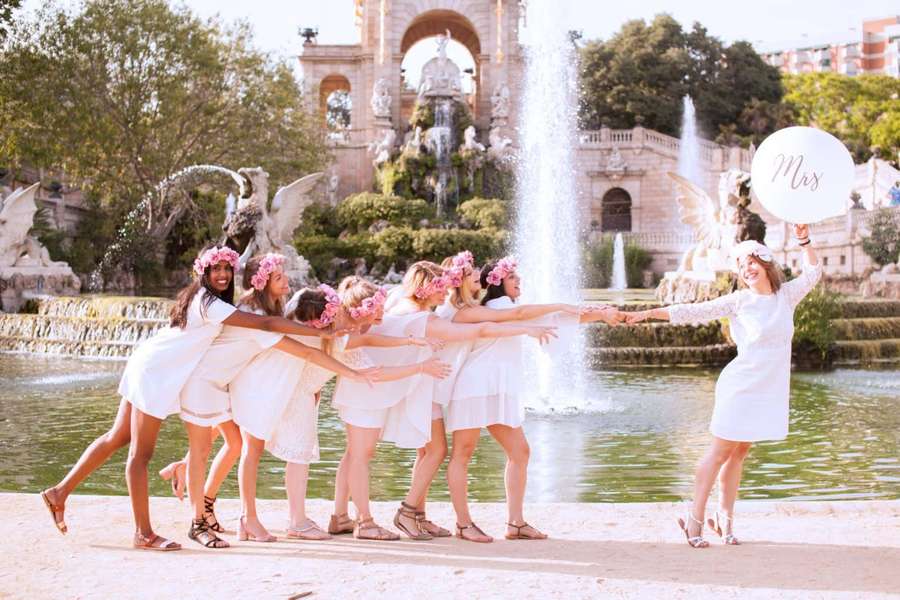 Women in white dresses and pink flower crowns celebrating by a fountain. — Bridesmaids Background
